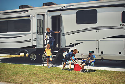 Four kids in front of a large, white RV on a sunny day with blue skiesn.